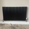 Black Designer Horizontal Oval Radiator Single Panel Black horizontal radiator installed with pipe connections visible