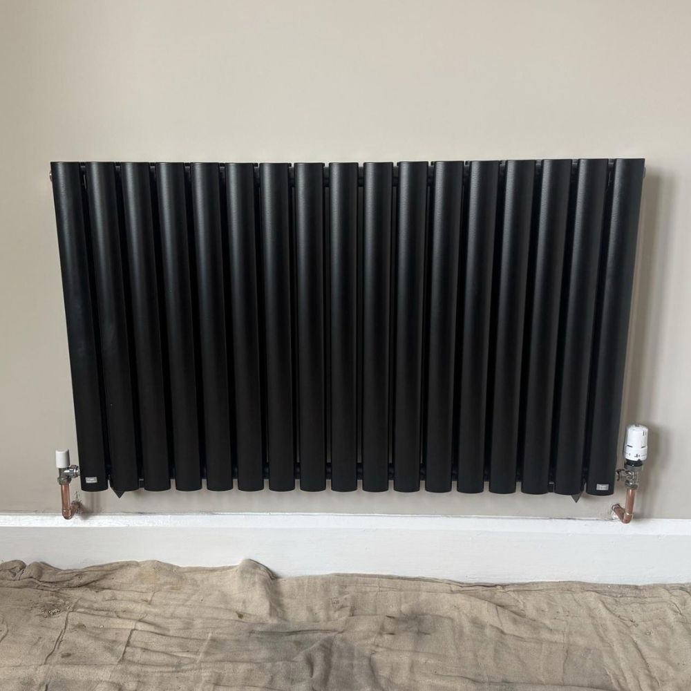 Black horizontal radiator installed with pipe connections visible